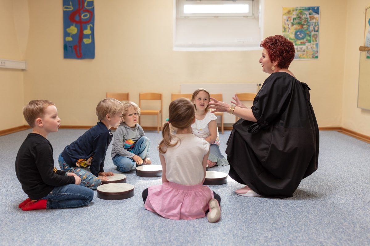 fünf Kinder mit trommeln vor sich, eine Pädagogin, die etwas erklärt