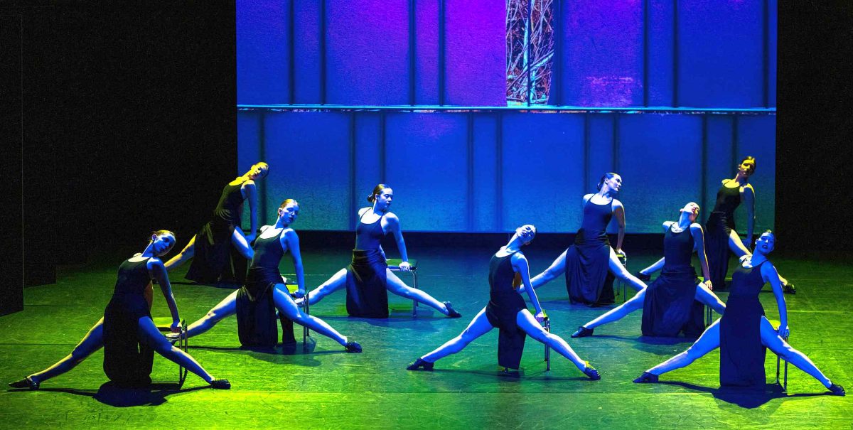 neun Tänzerinnen, die in Formation stehen, blaues und grünes Licht