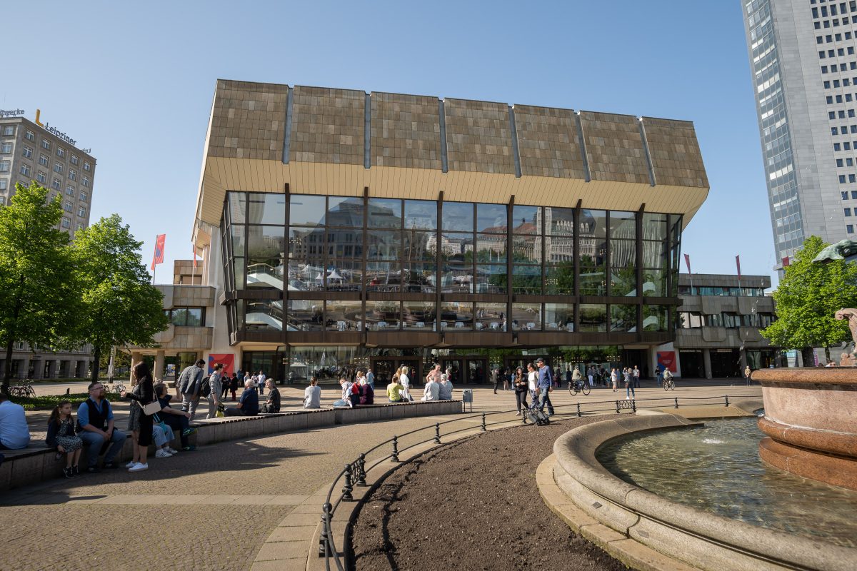 das Gewandhaus, ein modernes Gebäude im 70er Jahre-Stil mit einer großen Fensterfront, im Vordergrund sieht man ein Stück des Mendebrunnens