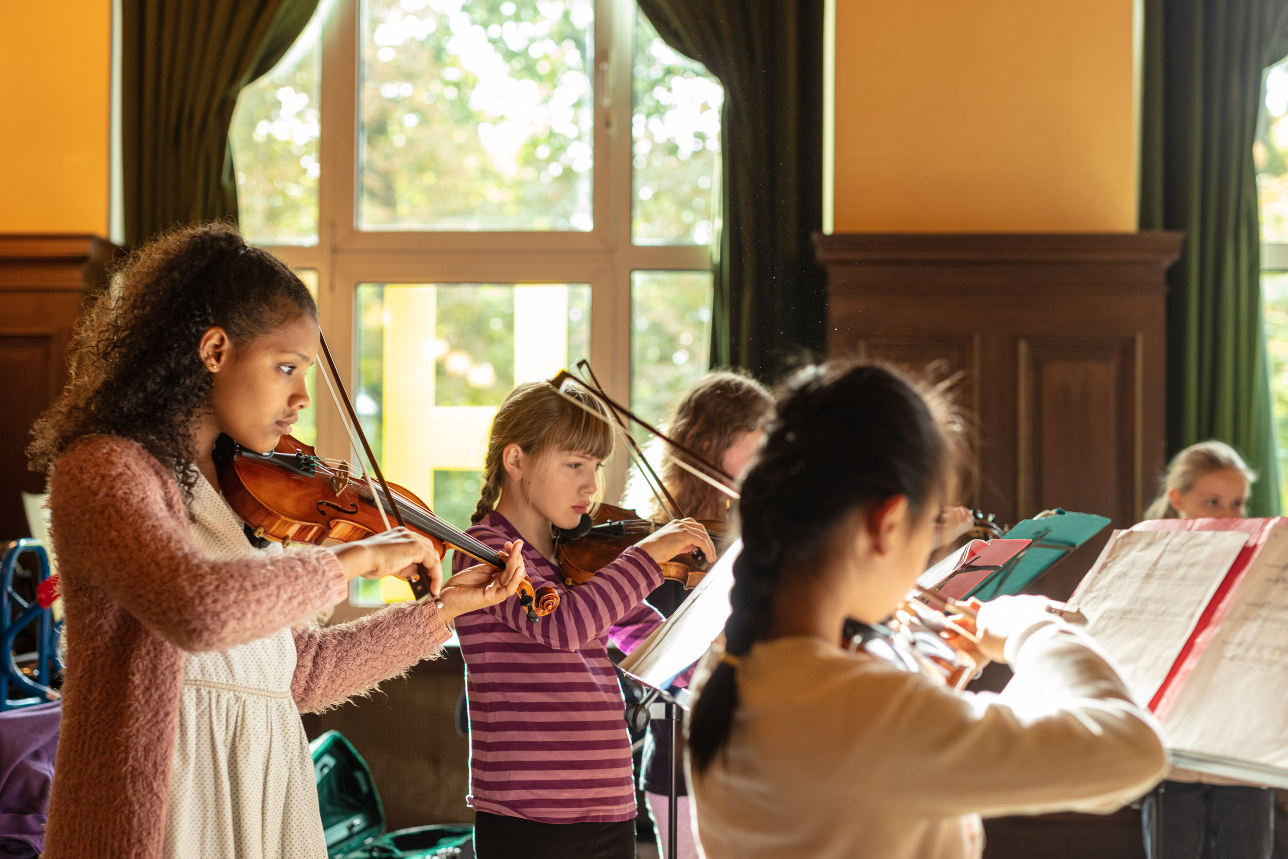 eine Gruppe aus fünf Mädchen spielt Instrumente, im Vordergrund sind drei Mädchen, die Violine spielen
