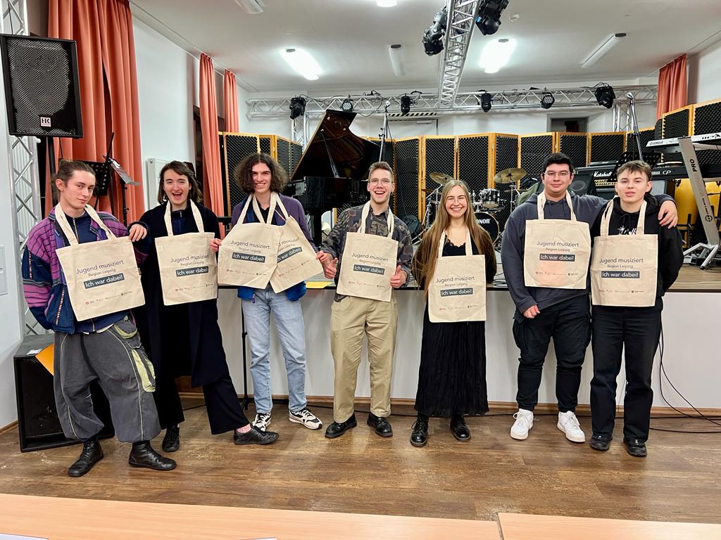 Schüler:innen stehen vor einer Bühne und halten Beutel mit der Aufschrift "Jugend musiziert-Ich war dabei"